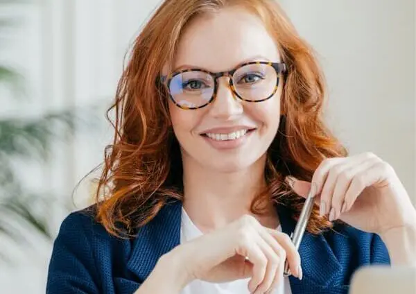 A woman in professional attire smiling and making eye contact with the camera, projecting confidence and positivity.