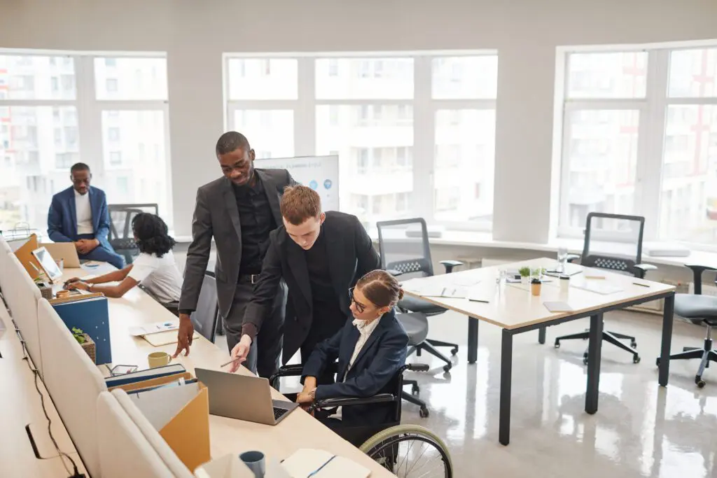An inclusive group of business people is shown in this image, working collaboratively in a modern office environment. The individuals are engaged in a discussion and appear to be sharing ideas and insights with one another. This image also relates to AI in recruitment, as many businesses are using AI-powered tools to promote inclusivity and diversity in their hiring processes. By leveraging AI, businesses can identify and remove any unconscious bias from the recruitment process, resulting in a more diverse and inclusive workforce.